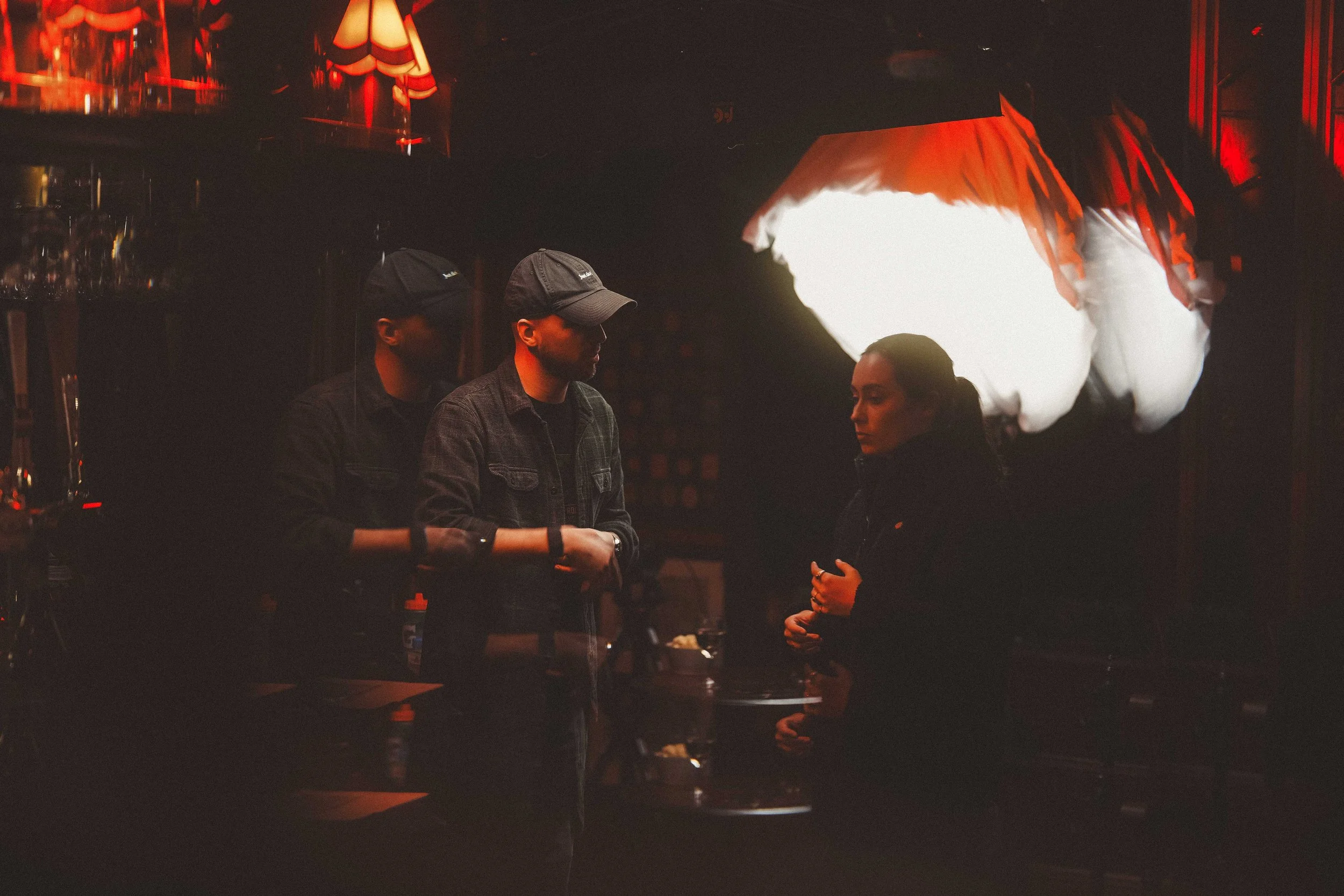 People standing around a bar counter inside a dimly lit venue with red and white lighting effects