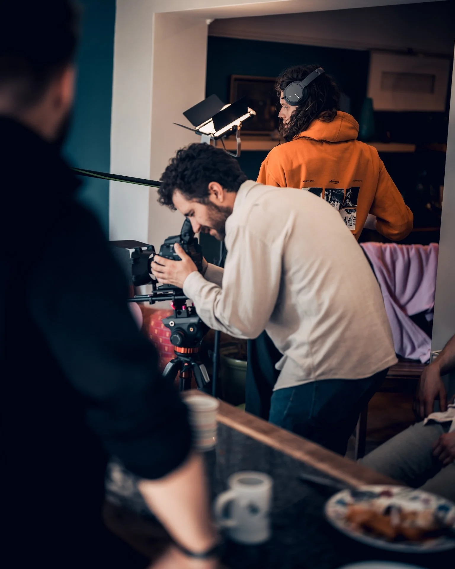 People working behind the scenes on a film or video shoot, with a woman wearing headphones and a man adjusting a camera.
