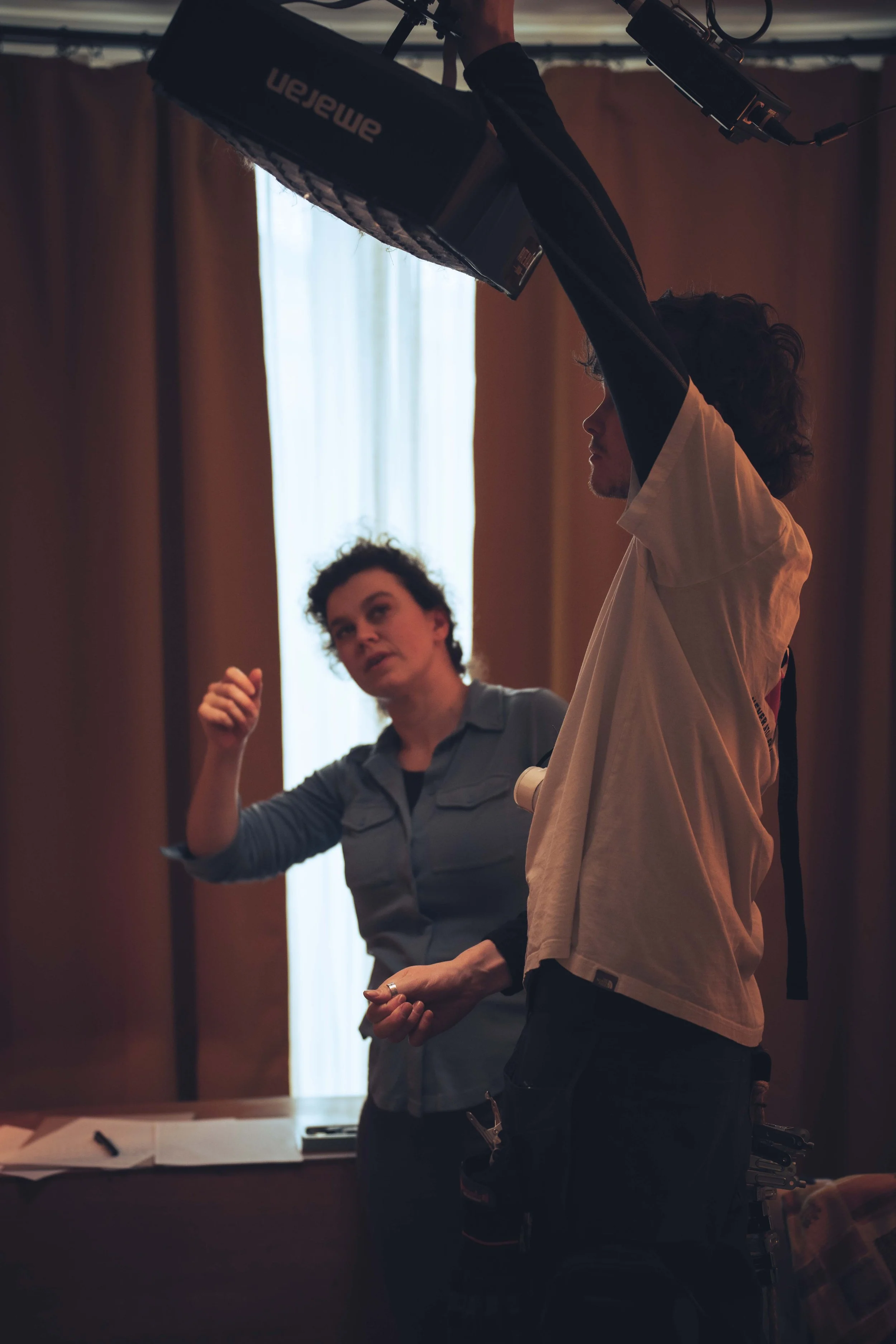 Two people engaging in a discussion or activity indoors, with one person holding a piece of equipment or a prop above their head.