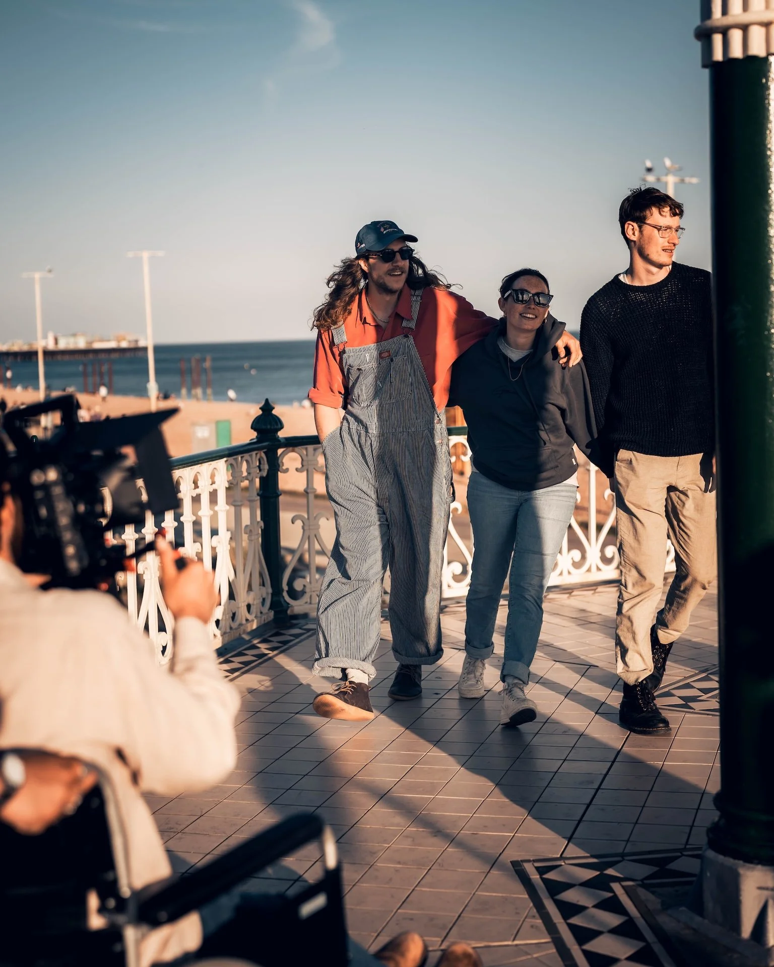 Three people walking on a balcony by the beach, with a camera and a person taking their photo in the foreground.