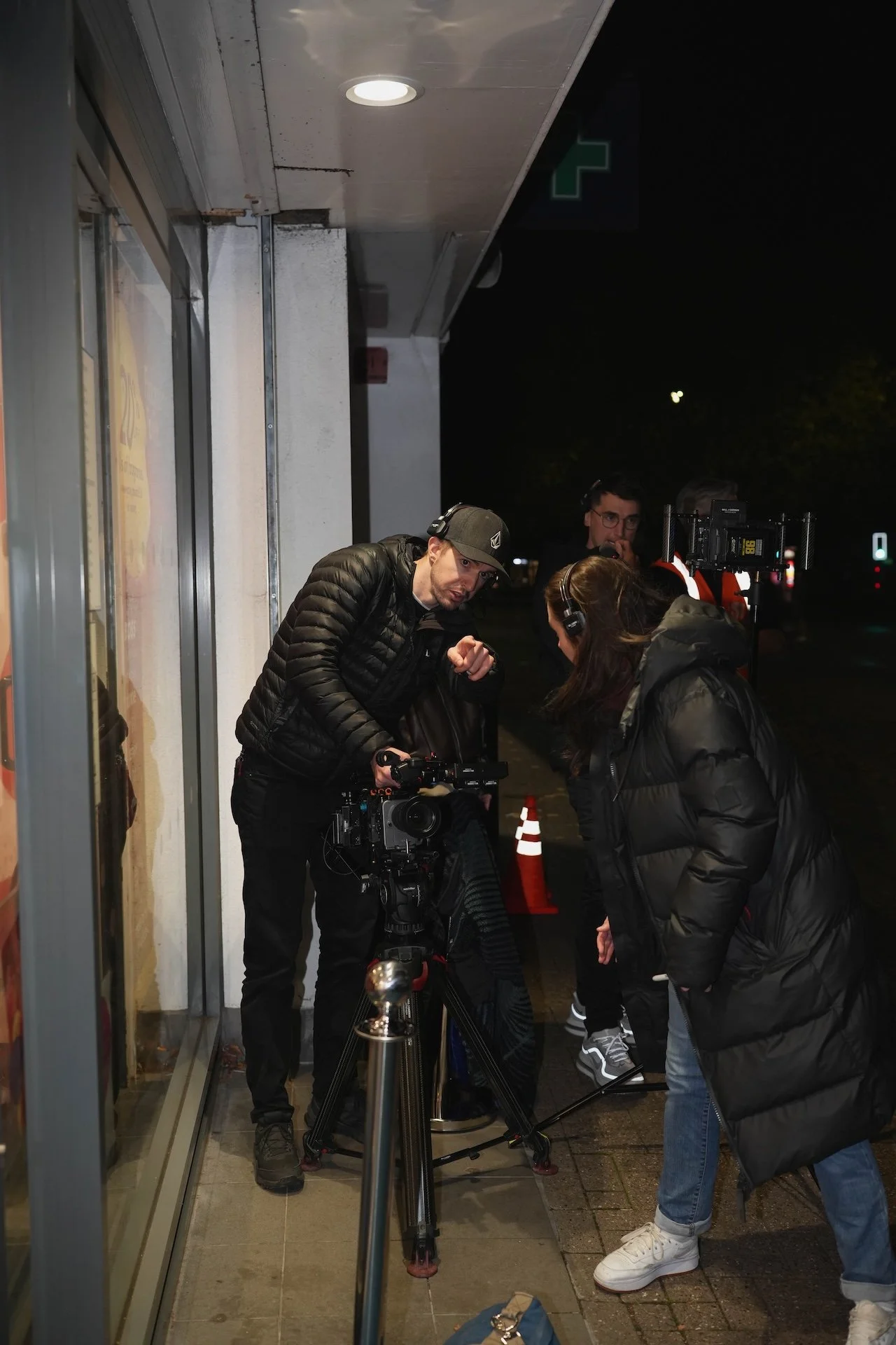Group of people filming or taking photos at night outside a building, with a person behind a camera on a tripod, and others examining equipment or discussing.