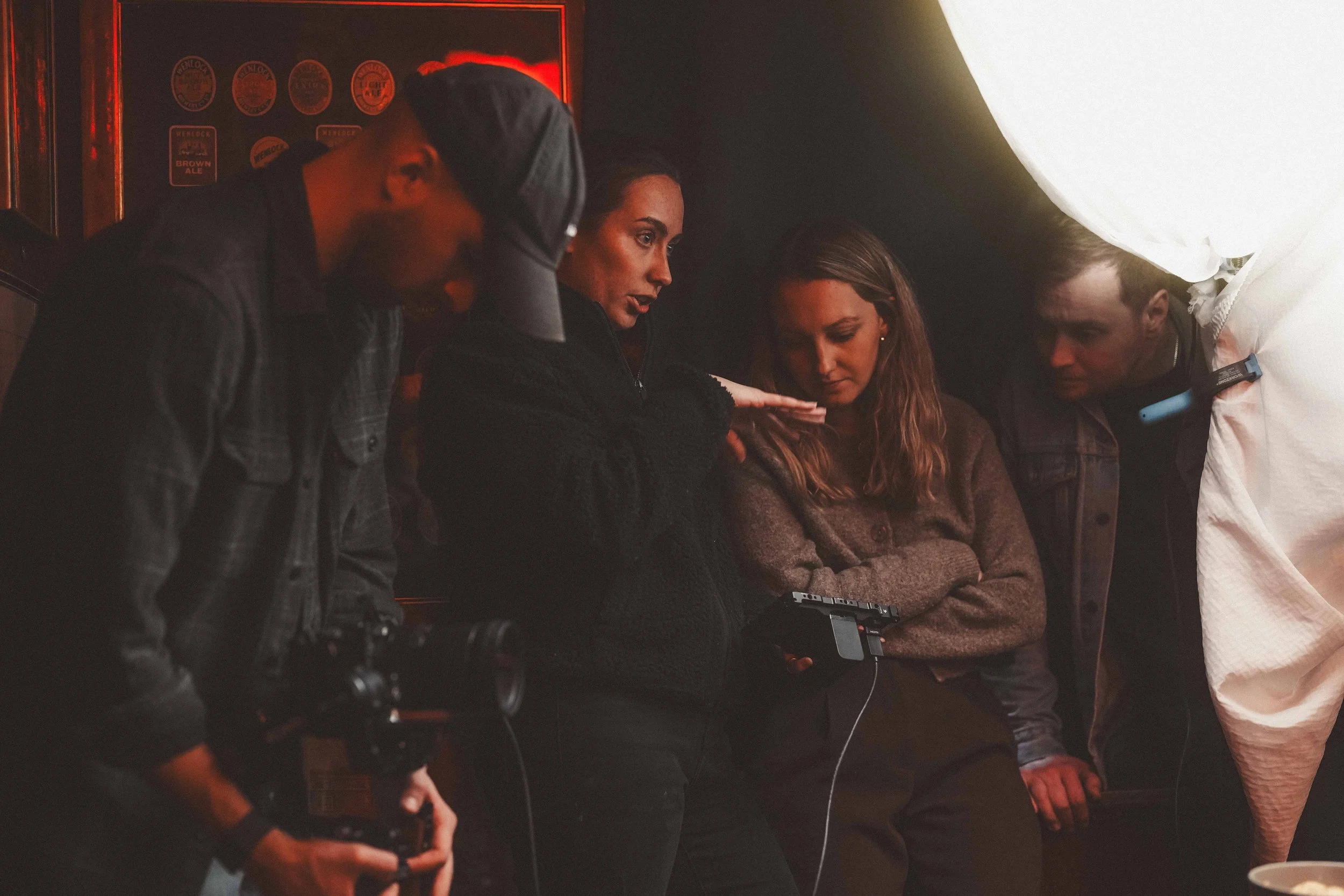 Four individuals in a dimly lit room, with three women and one man, engaging in a conversation or activity together. The scene includes a large illuminated white object or structure on the right side.