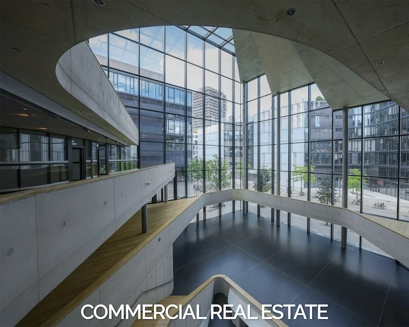 Interior of a modern commercial building with glass walls, curved walkways, and a city street view outside.