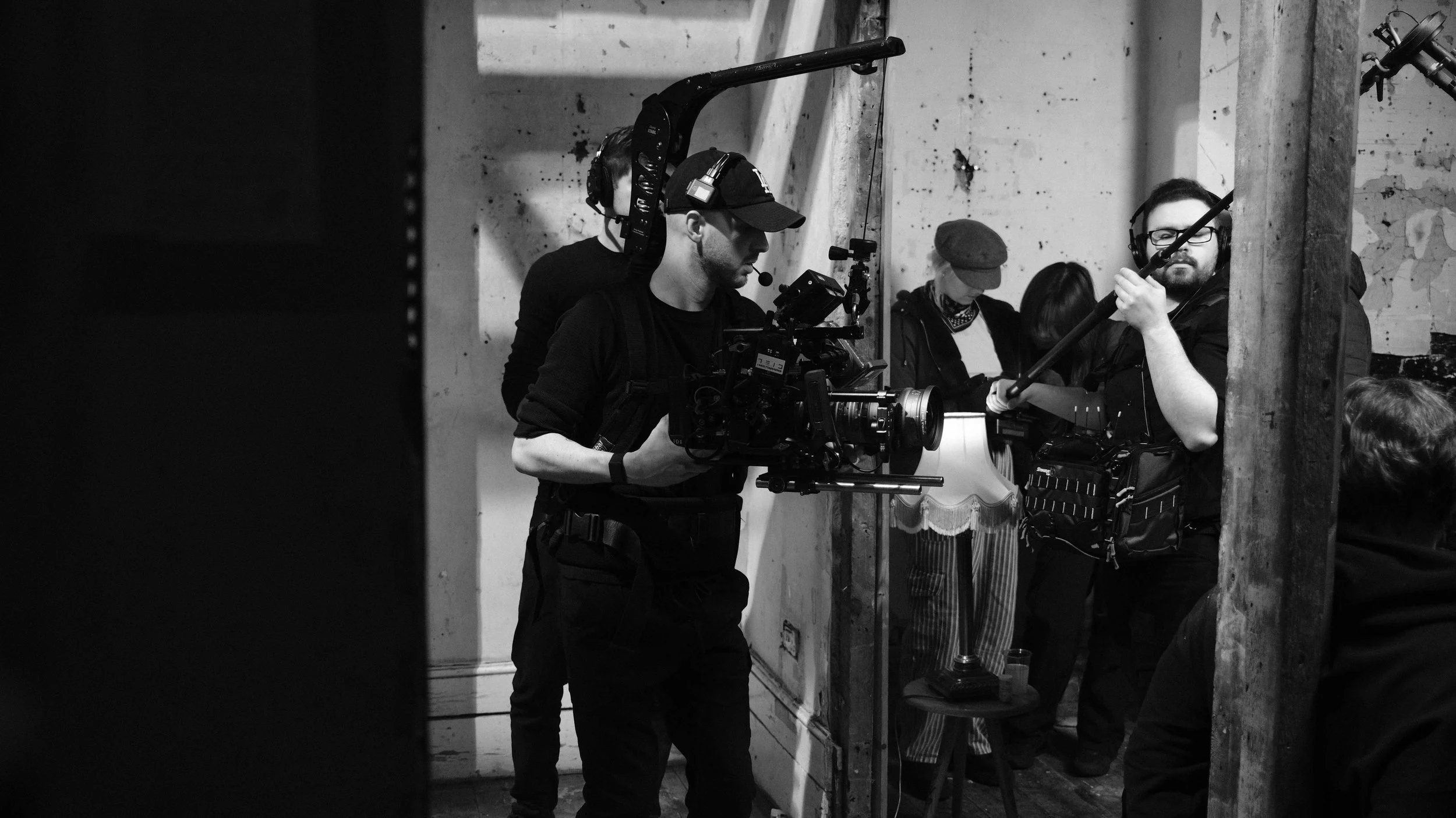 Filmmakers and crew working on a production set, with one person operating a professional camera and others setting up equipment in a behind-the-scenes shot.