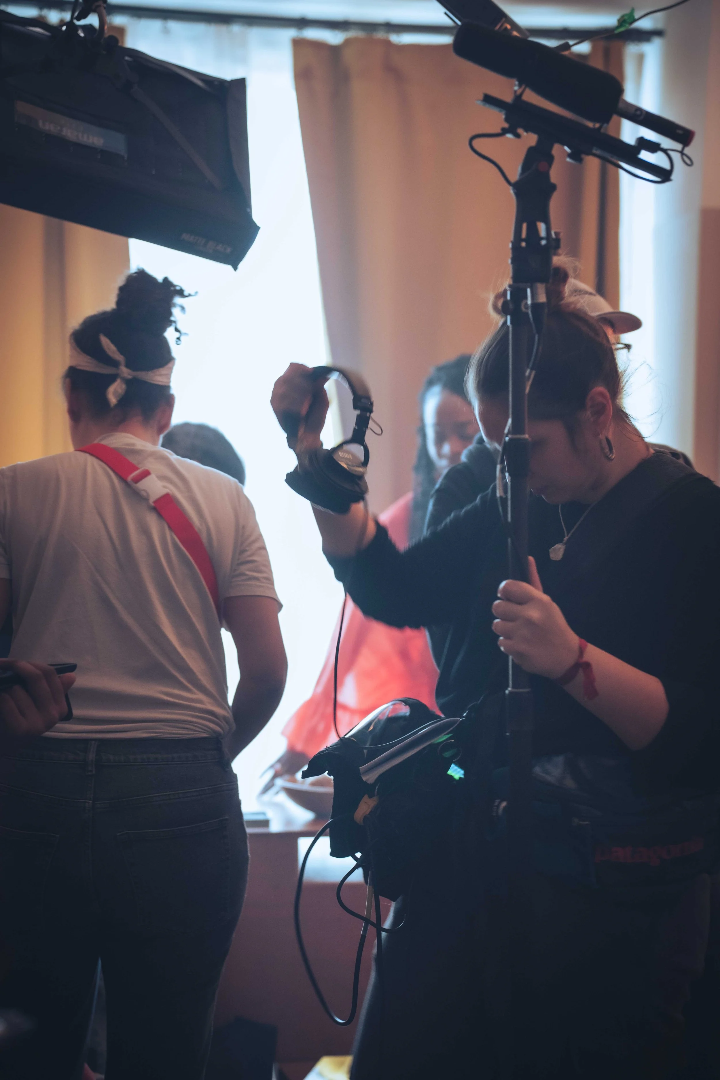 People working on a film or video shoot indoors, with camera equipment, cables, and lighting in view.