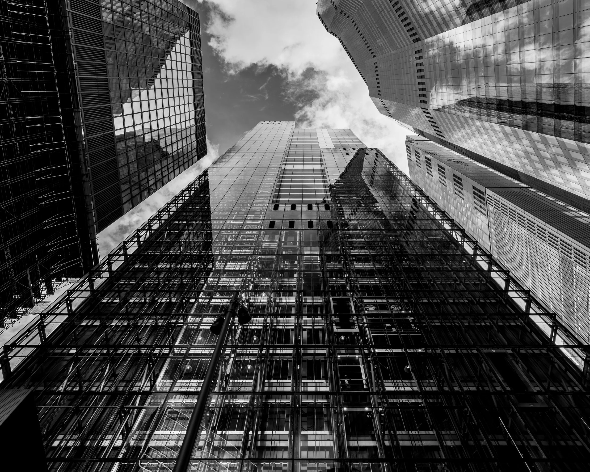 Low-angle view of tall modern glass skyscrapers in a city, with clouds visible in the sky.