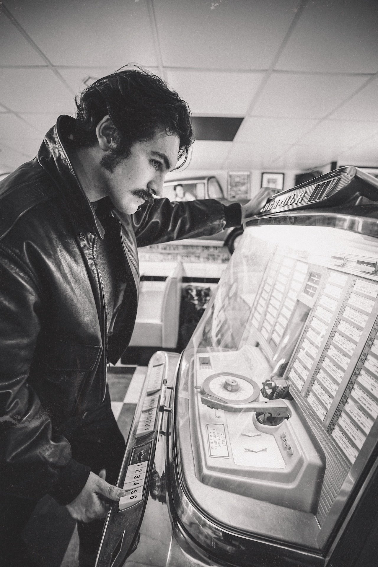 A man in a leather jacket using a vintage jukebox in a record store or arcade.