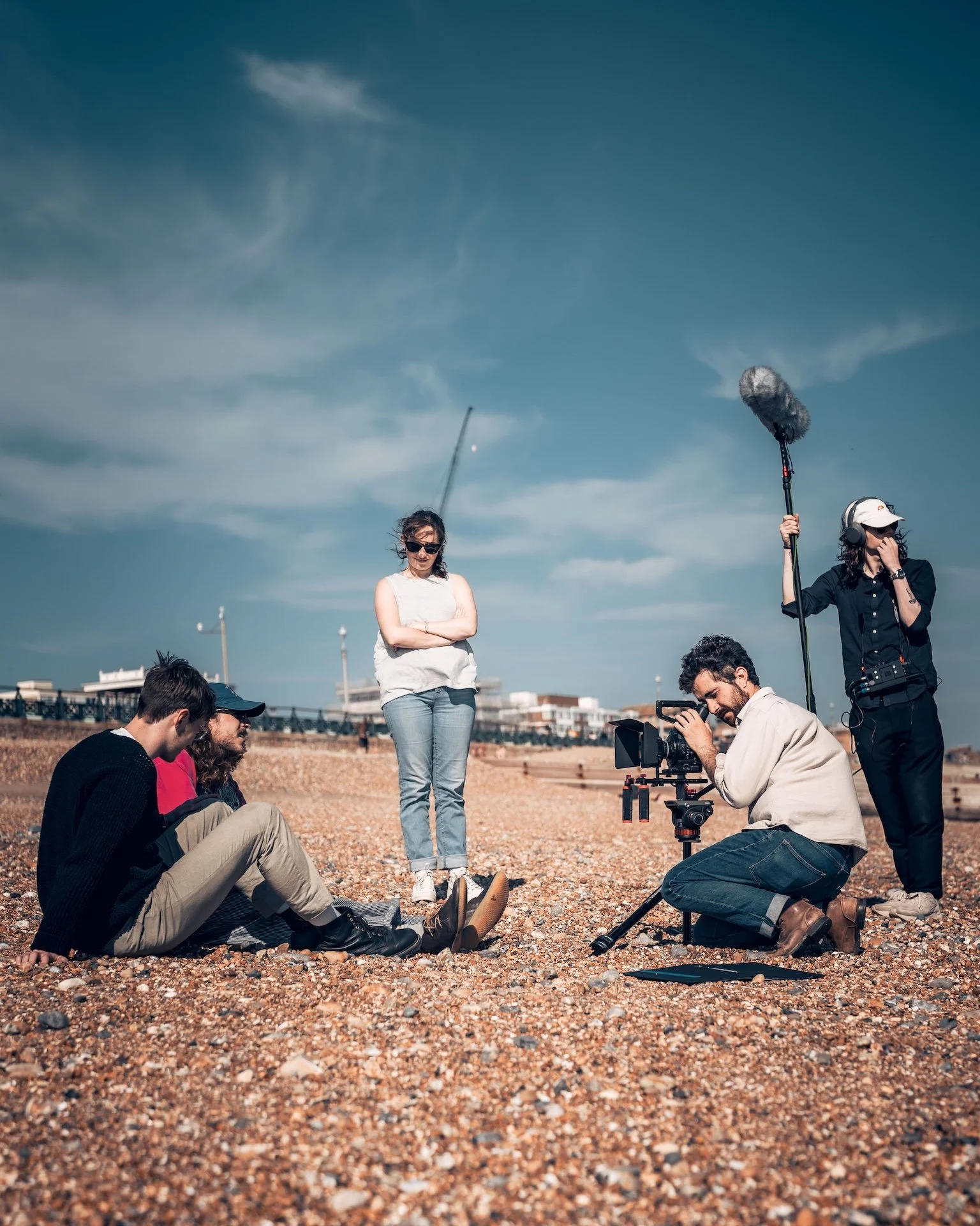 Film crew filming a woman on a rocky outdoor location under a blue sky.