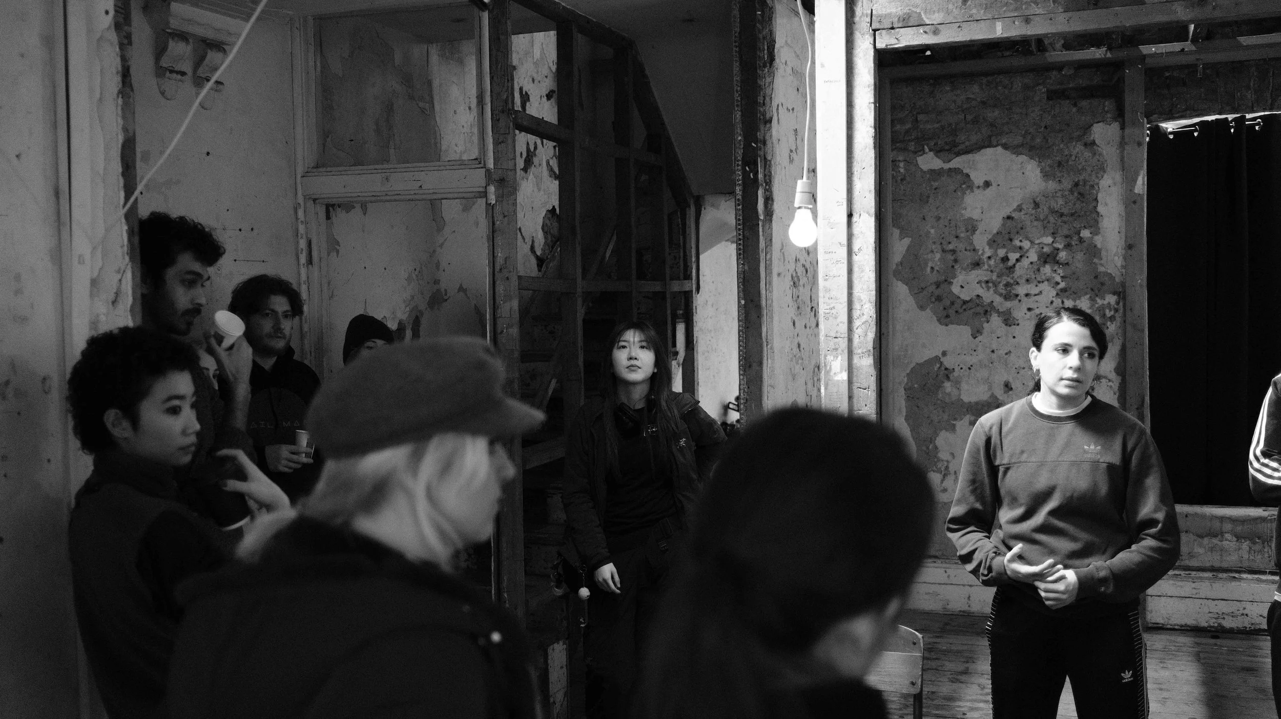 A group of people gathered in an industrial-style room with exposed brick and unfinished wood, listening to a woman who appears to be speaking or presenting.