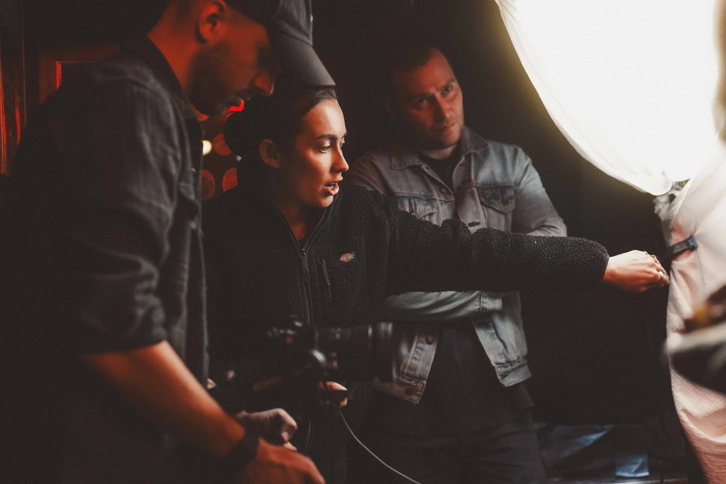 A group of four people sitting closely together, engaged in a conversation or activity, in a dimly lit setting.