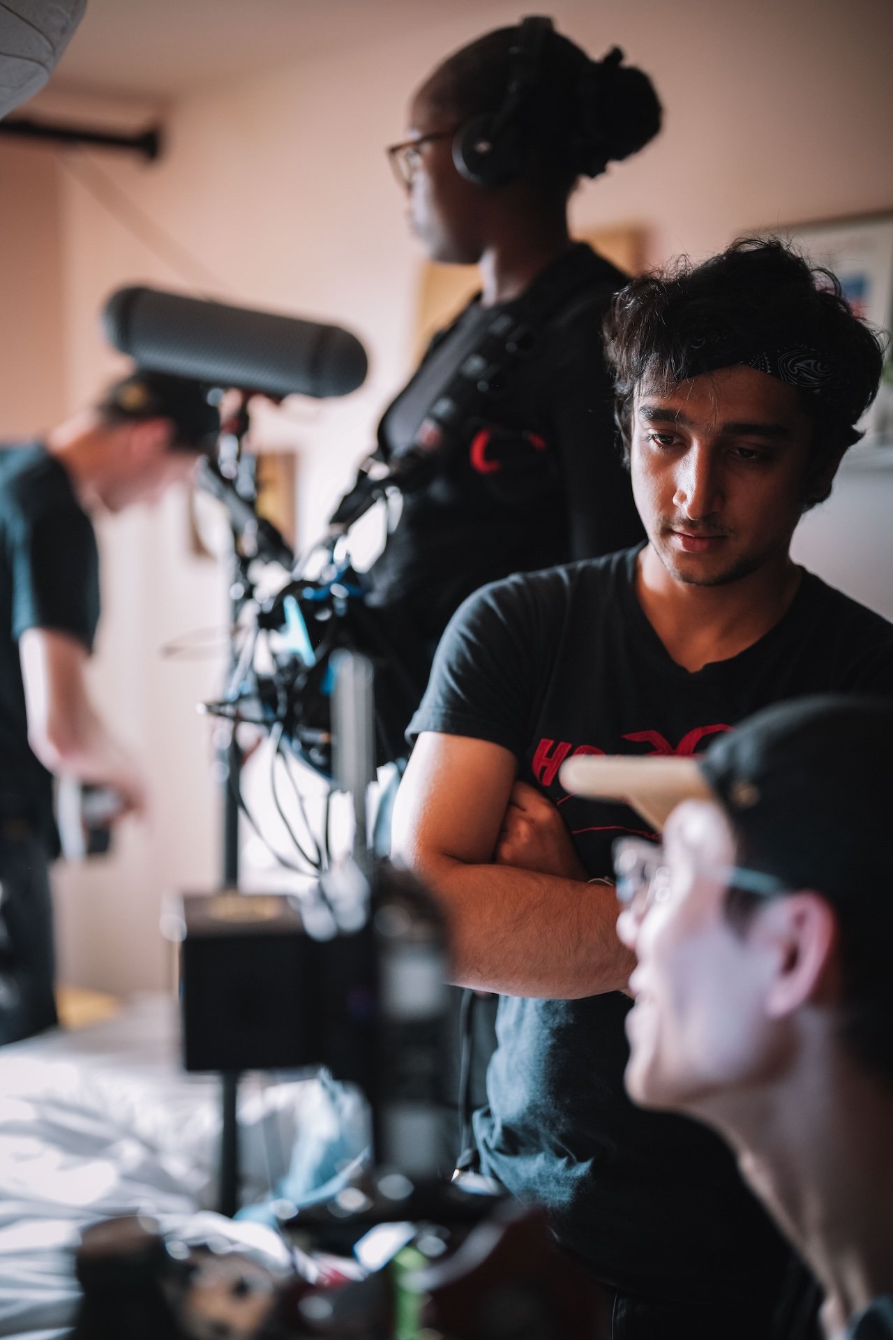A group of young people engaged in filming or photography, with one person in focus looking at a device, and others working with cameras and equipment in a room.