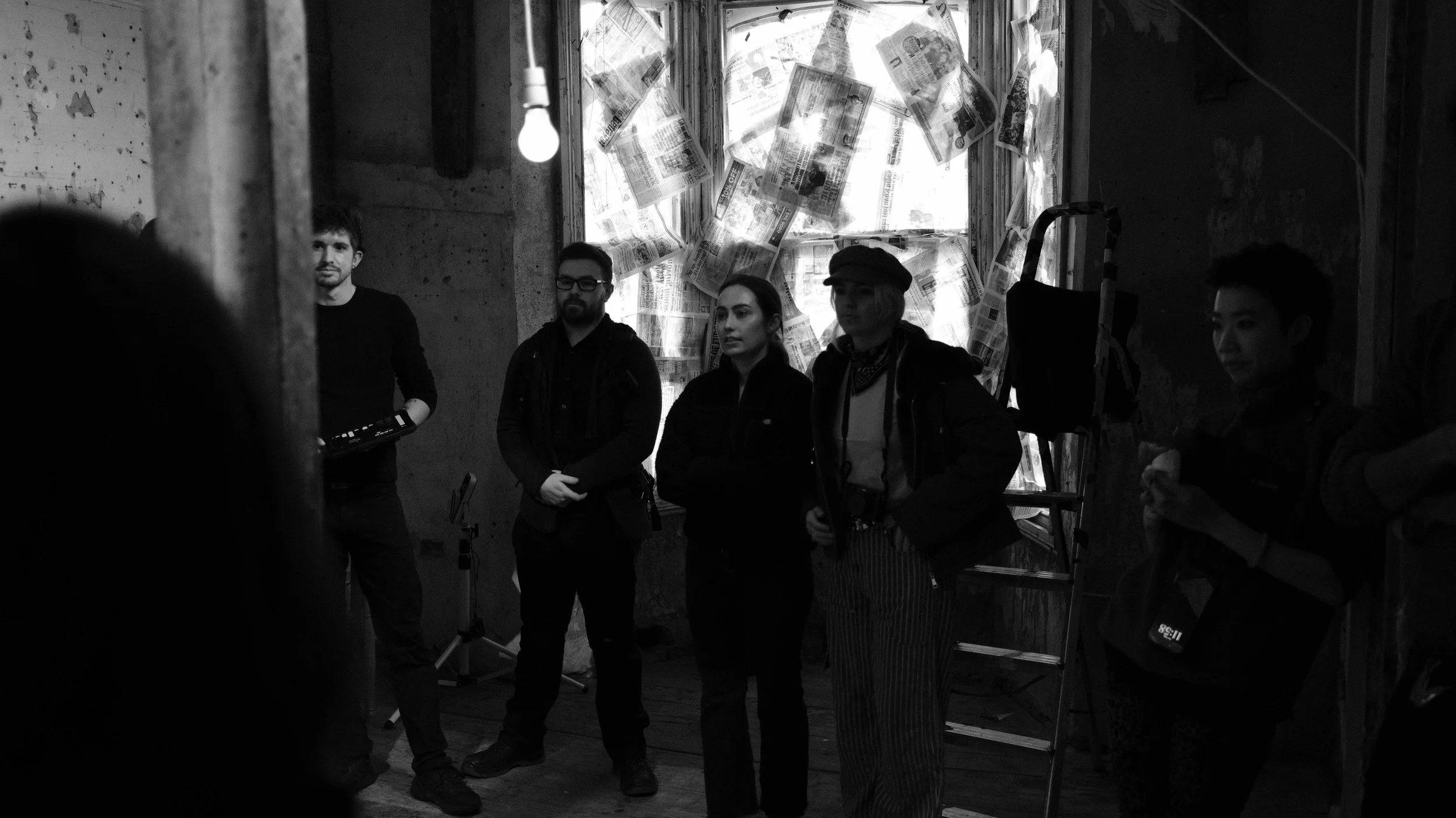 A group of five people standing inside an indoor space with a paper-covered window in the background, black and white photo.