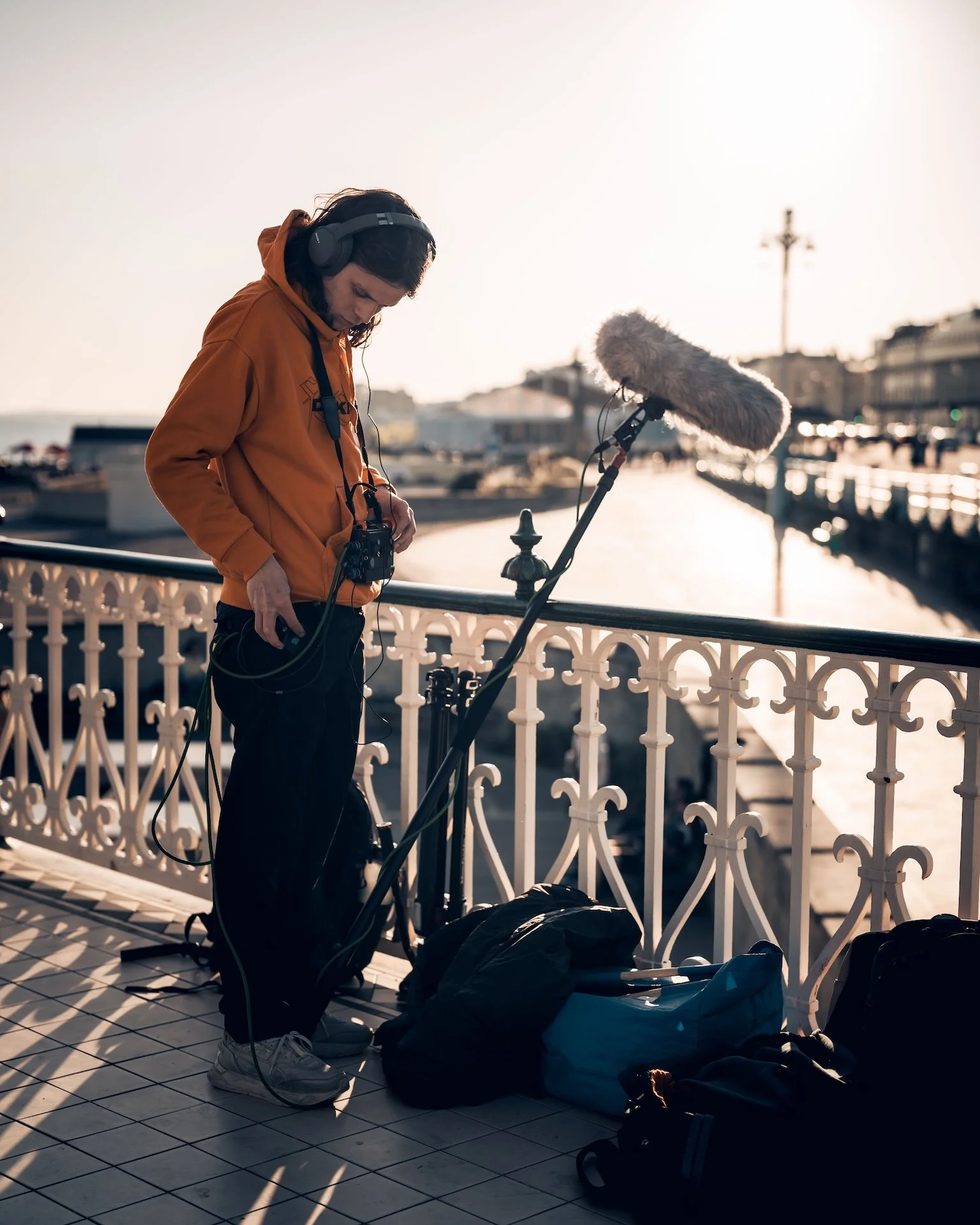 A woman with headphones and a camera, setting up audio equipment on a seaside balcony during sunset.