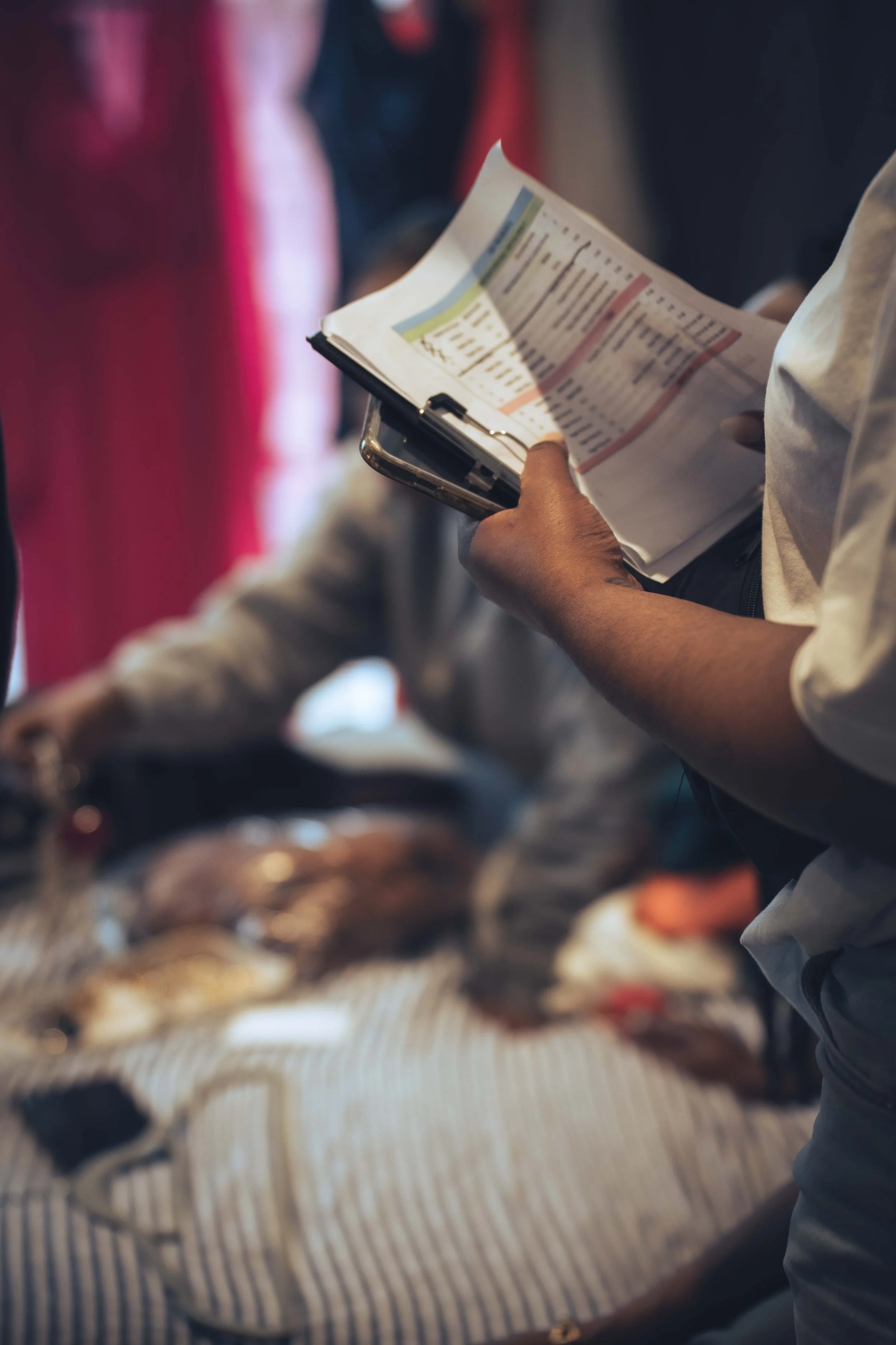 Person holding a sheet of paper with colored bars, standing near a table with pastries, others blurred in the background.
