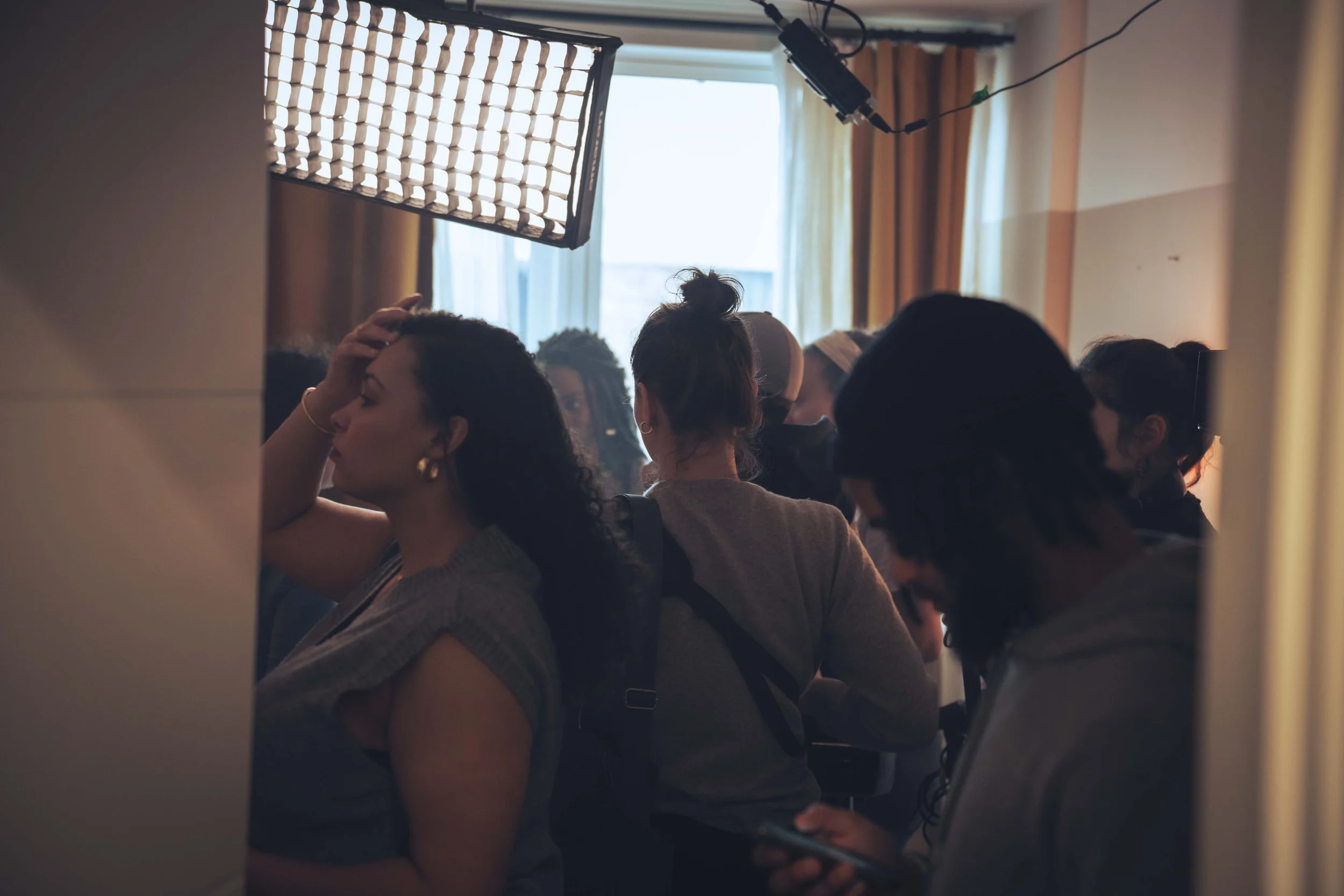 Group of women sitting in a room with natural light coming through the window, some with head coverings and hair tied up, appearing to be engaged in an activity or discussion.