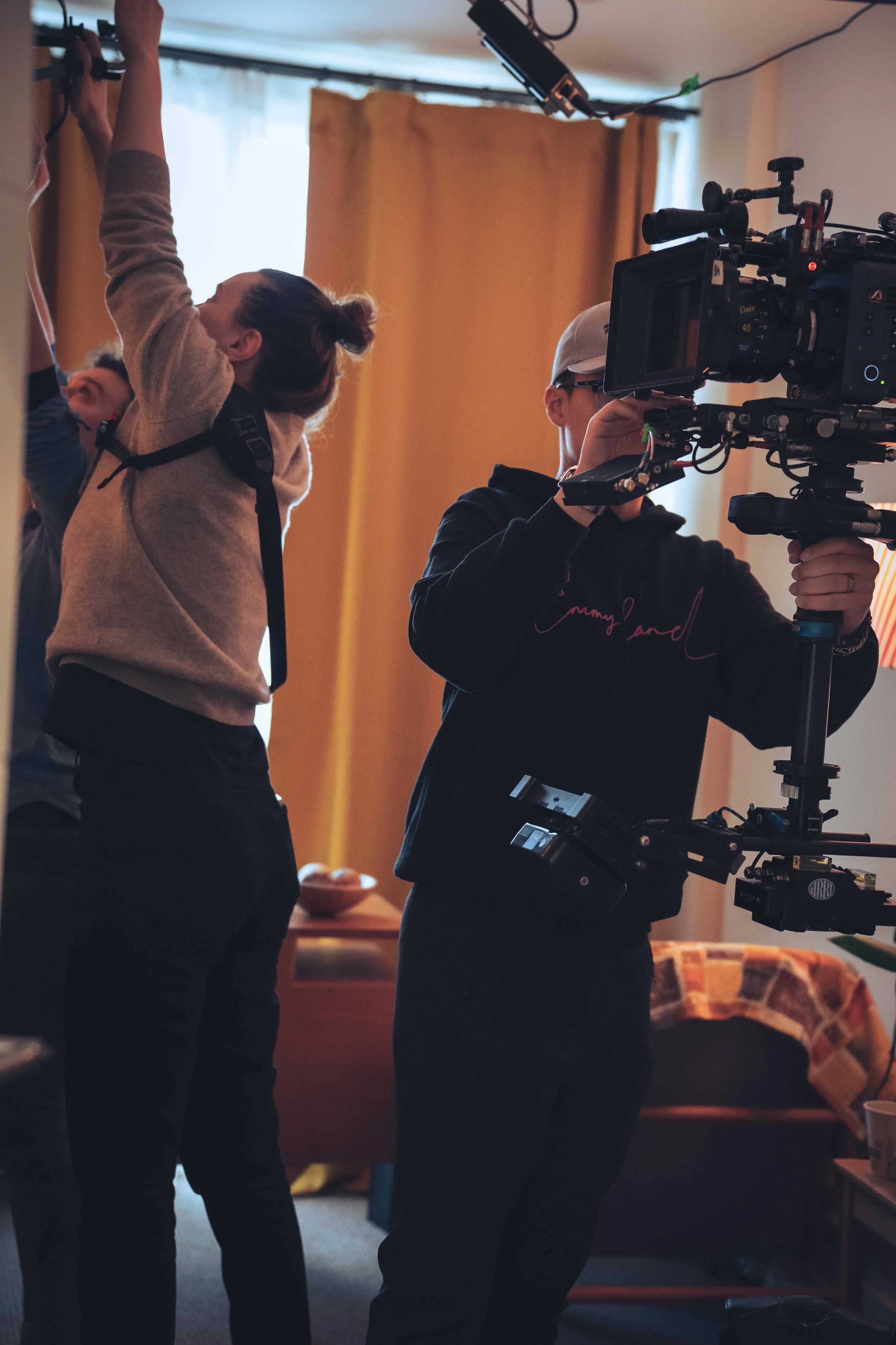 People working with film equipment and a camera inside a room with curtains.