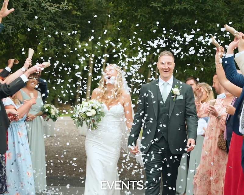 Bride and groom happily walking as confetti is thrown over them during their wedding celebration, surrounded by guests.