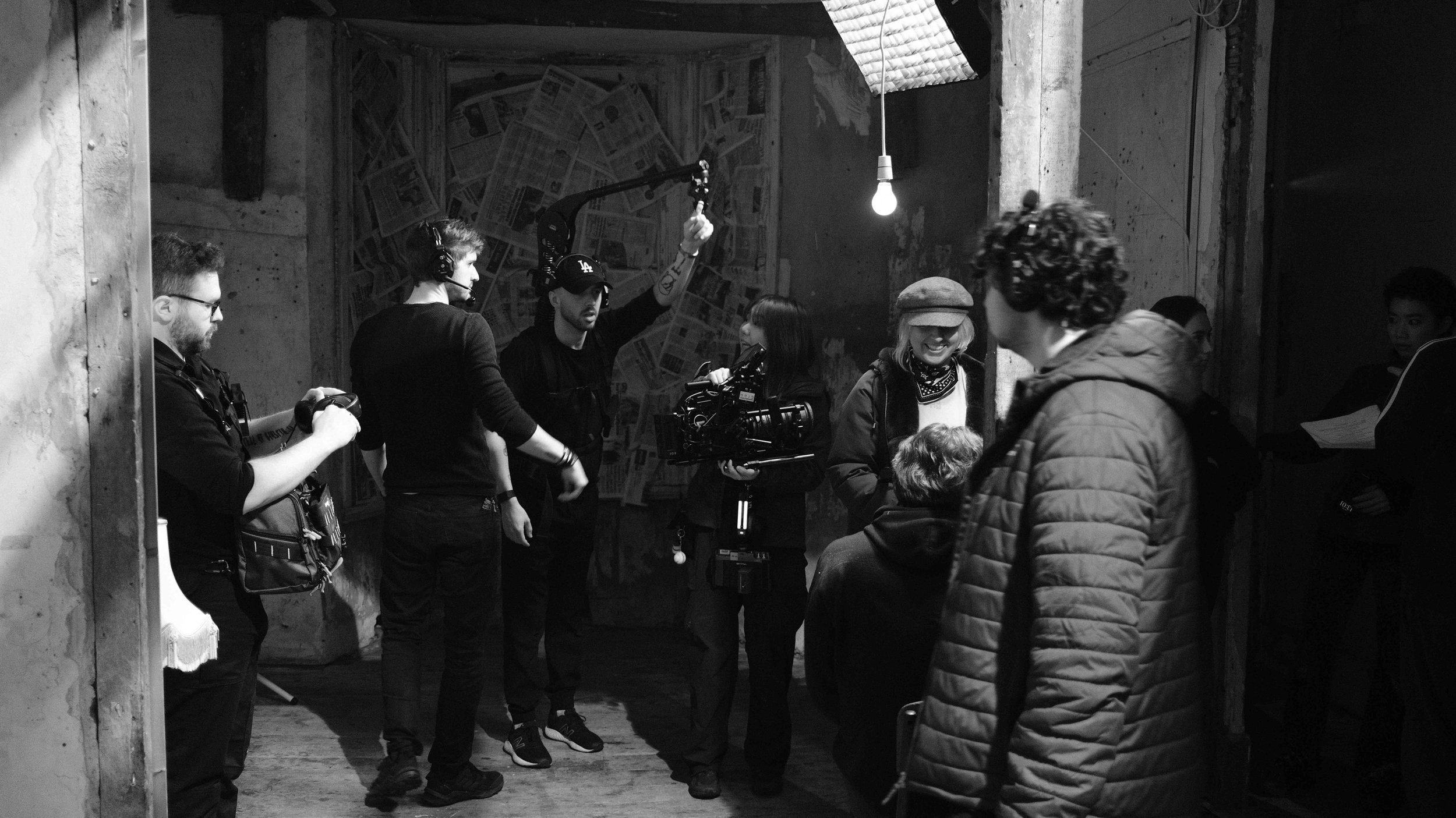 A film crew is filming indoors with crew members preparing equipment and lighting, and an actress smiling.