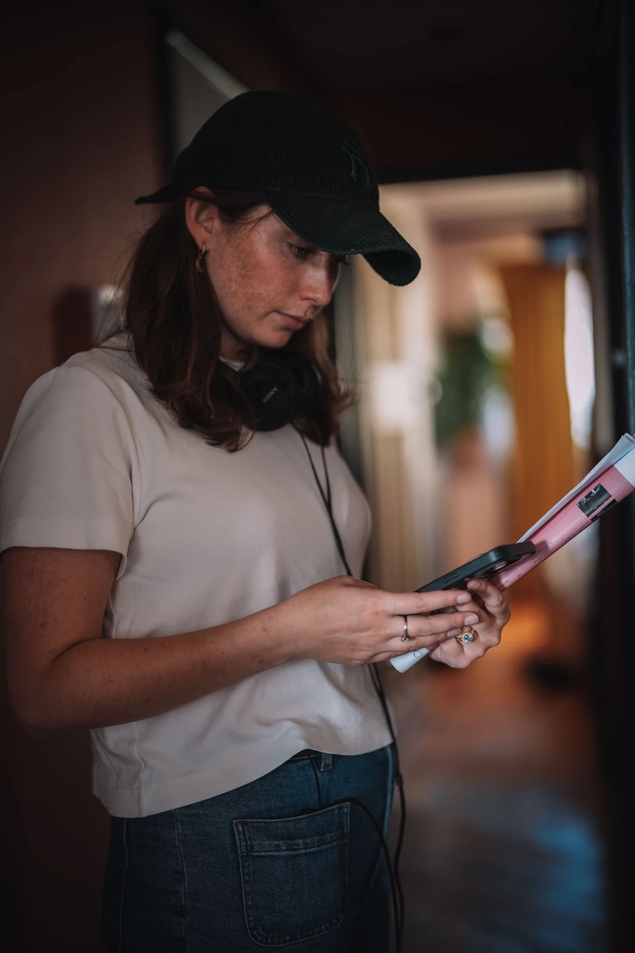 Young woman with freckles, wearing a black cap and a beige shirt, reads a tablet with documents attached, holding it in her hands.