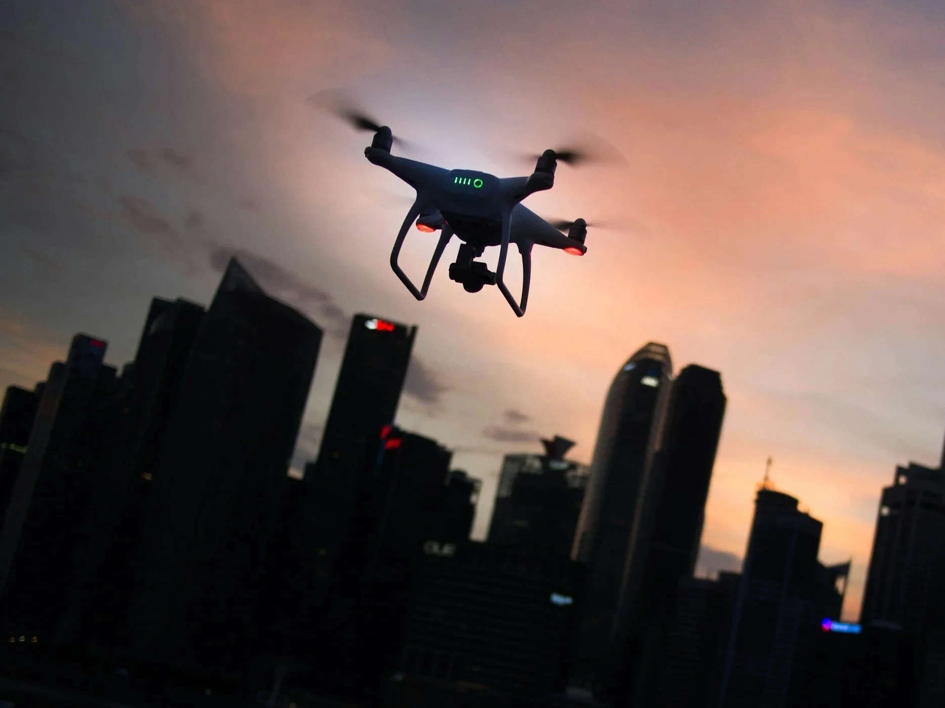 A drone flying in the sky over a city skyline during sunset.