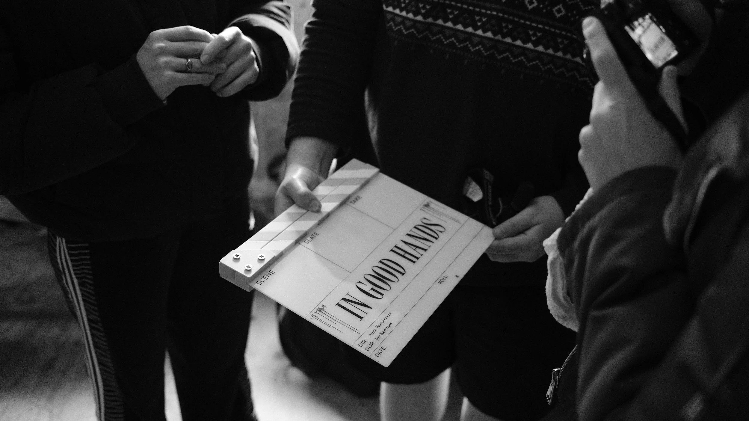 Three people on a film set discussion, one holding a clapperboard that reads, 'In Good Hands'.