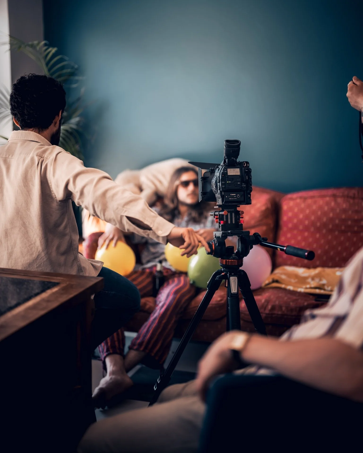 People filming a woman with sunglasses in a room decorated with balloons and a blue wall.