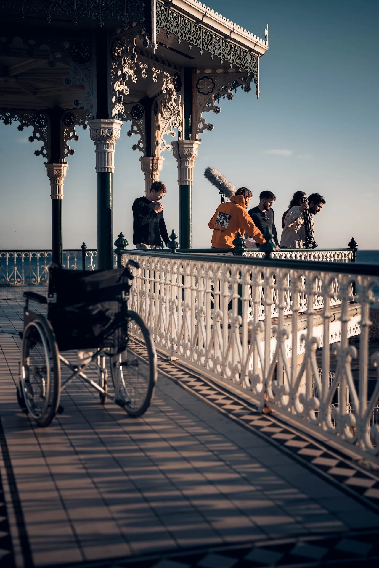 A bicycle parked on a promenade near a white ornate railing and a decorative pavilion, during sunset with a clear sky and ocean in the background.