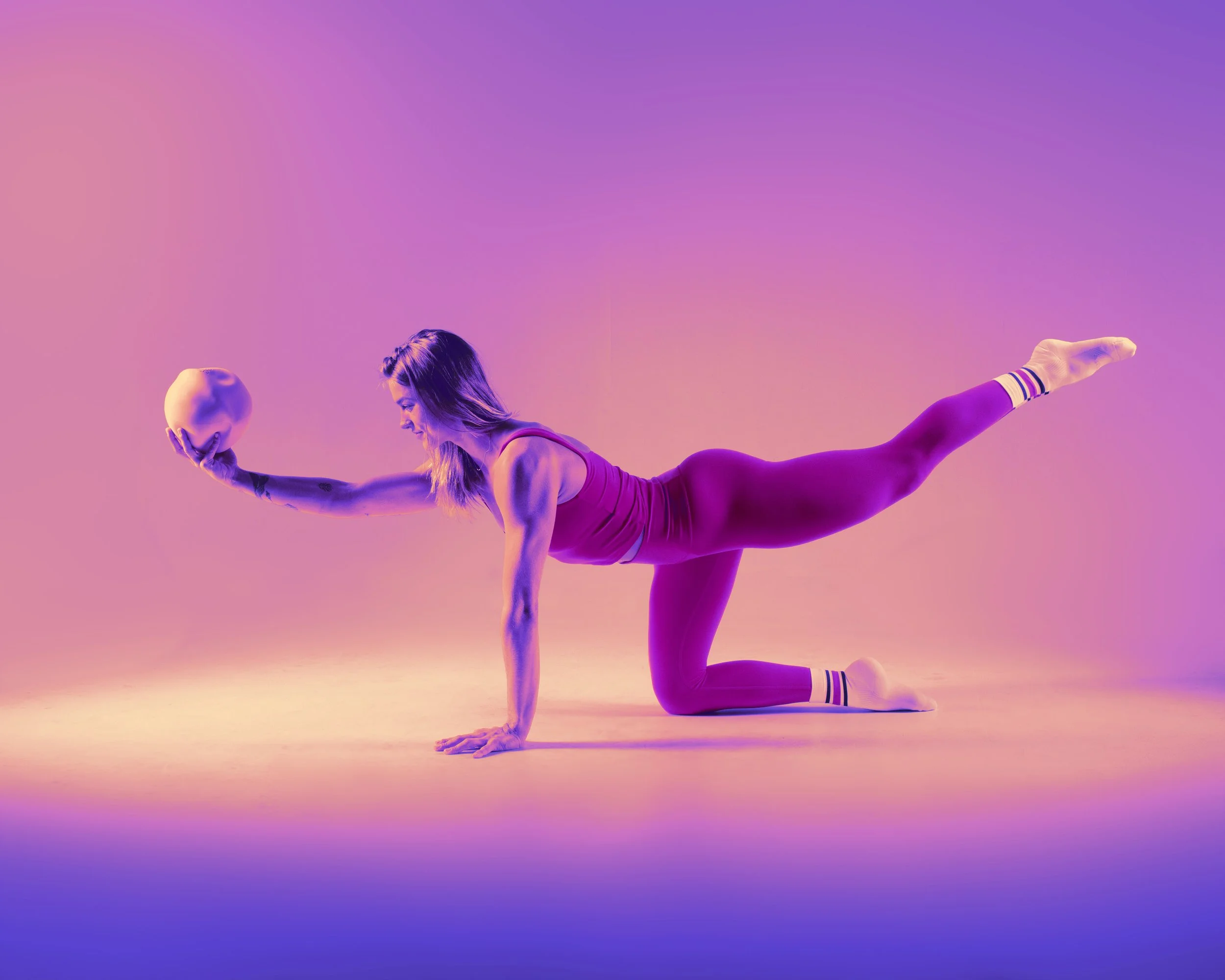Woman in fitness outfit performing a yoga pose with a ball against a pink and purple gradient background.