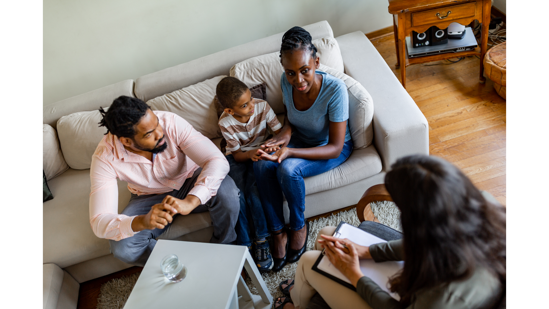 A diverse group of people having a serious conversation in a living room, with a counselor or therapist taking notes.