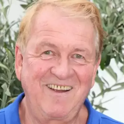 Nahaufnahme eines lächelnden Mannes mit blonden Haaren vor grüner Pflanzenumgebung.