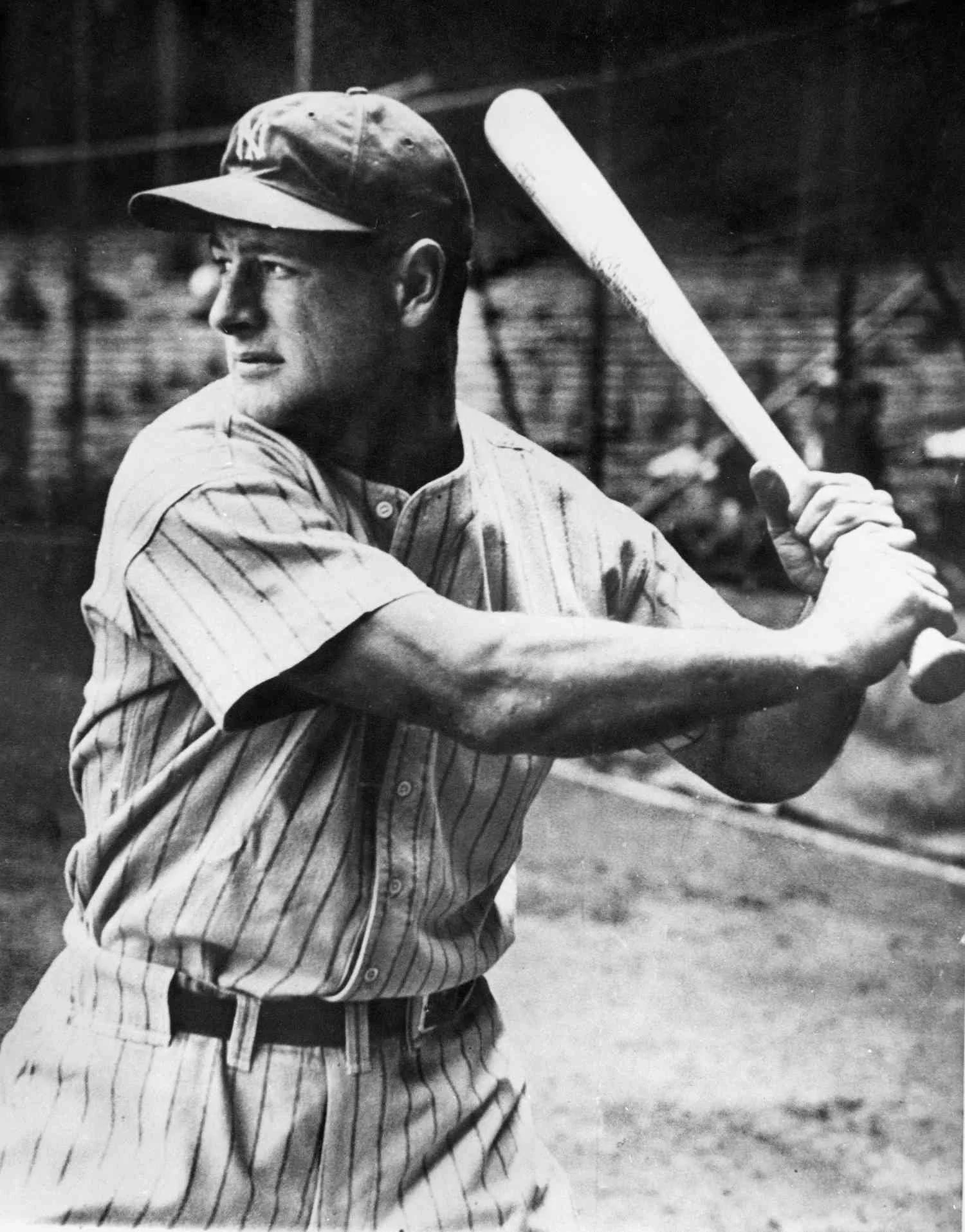 Black and white photo of a man in a baseball uniform holding a bat, preparing to swing, on a baseball field.