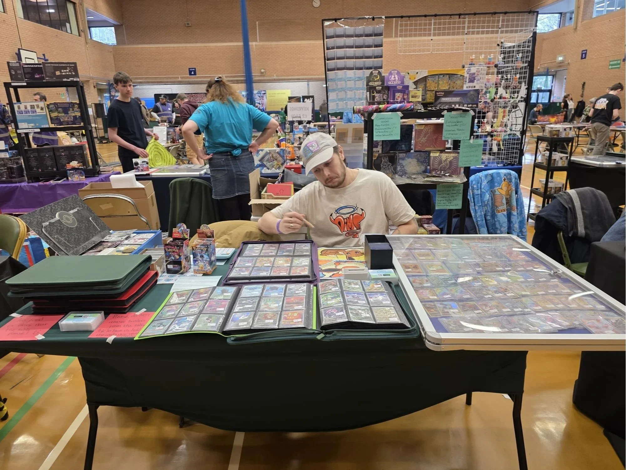 Radam's Poke Stop at Geek Mania Card show, a display of cards in binders on a table in a busy hall