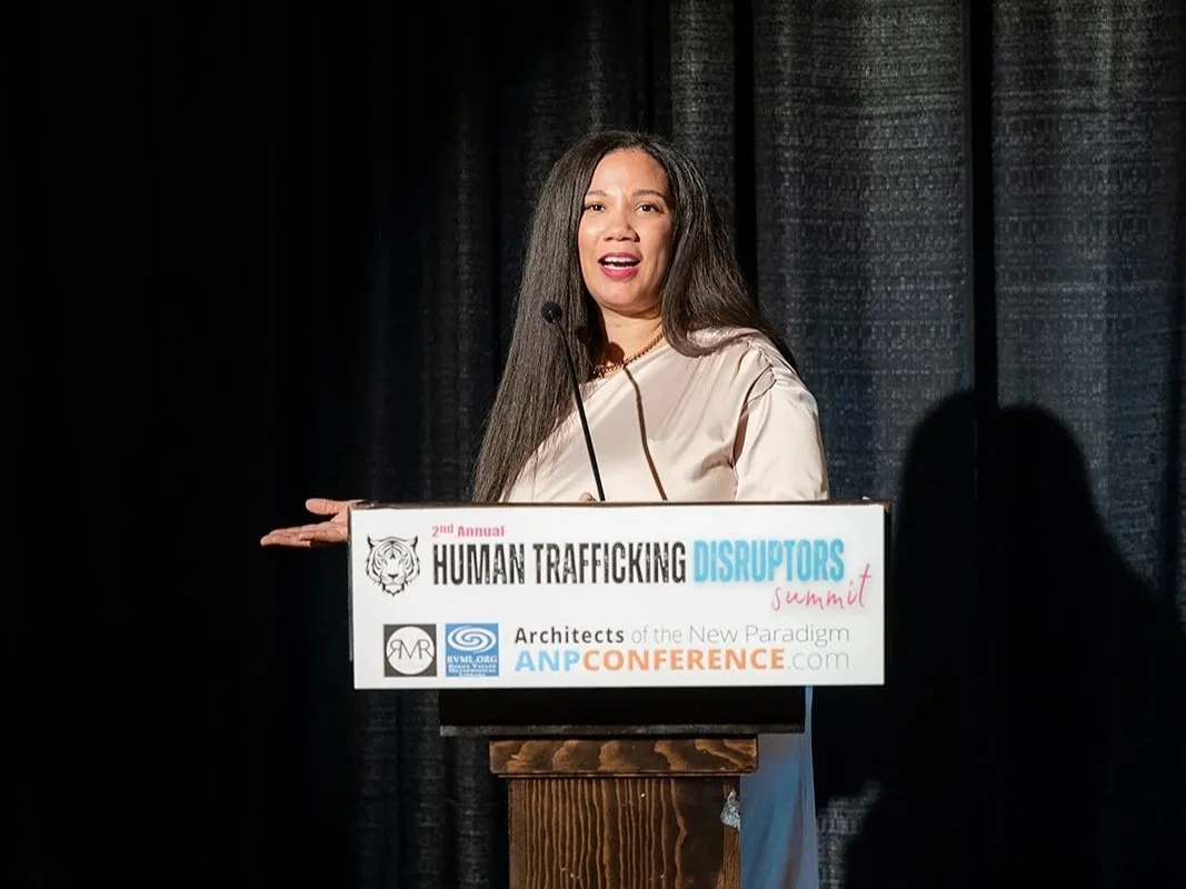 A woman speaking at a podium during a conference about human trafficking, with a black curtain in the background.