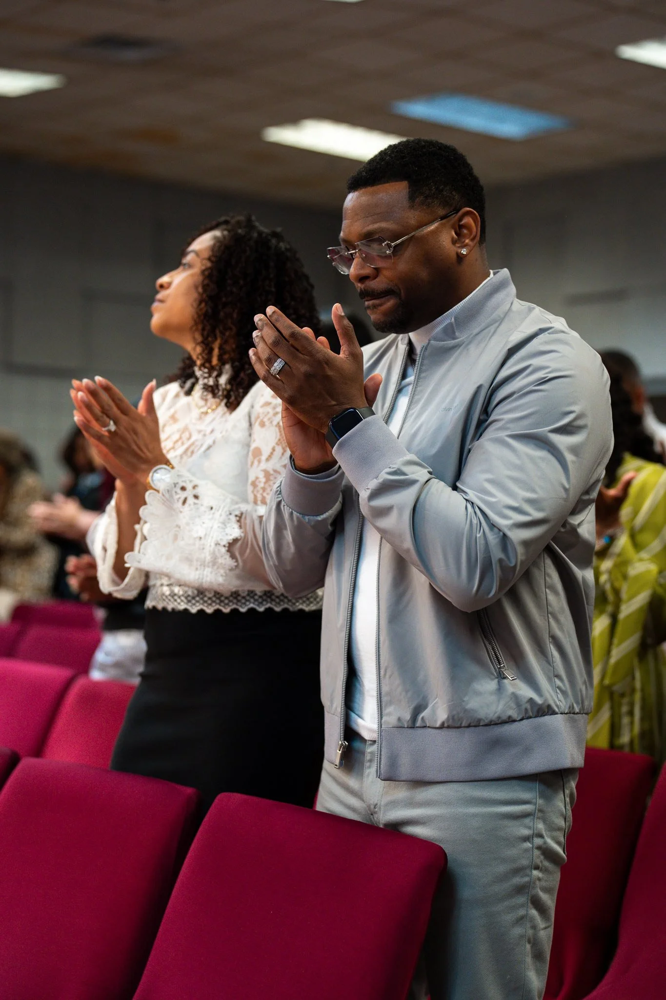 People praying in a church or conference setting, with hands clasped and eyes closed.