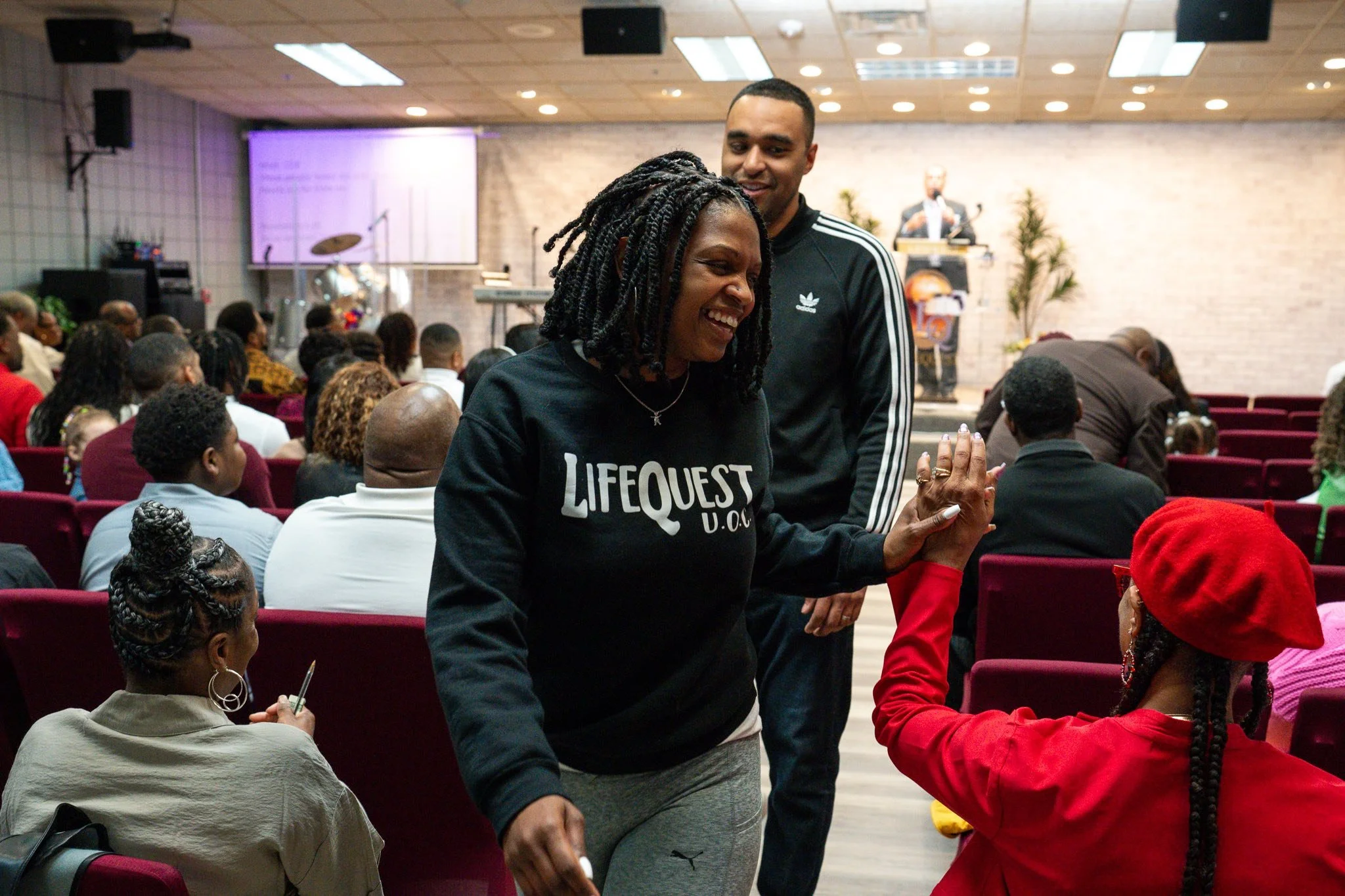A woman with dreadlocks smiling and giving a high five to a woman in a red beret in a crowded indoor event hall.