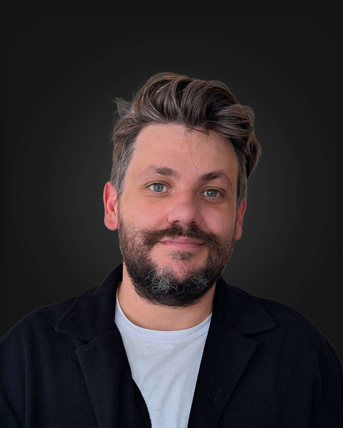 A portrait of a man with blue eyes, brown hair, and a beard, wearing a black jacket and a white shirt, smiling against a dark gradient background.