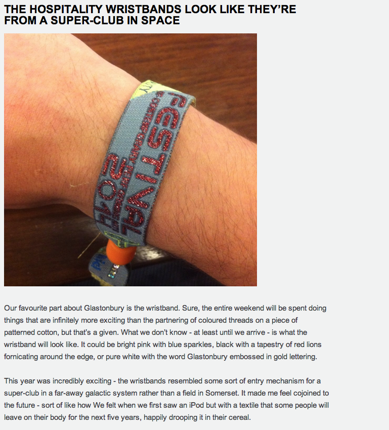 Close-up of a person's wrist wearing a fabric wristband with red and blue embroidery, possibly from an event, resting on a wooden surface.