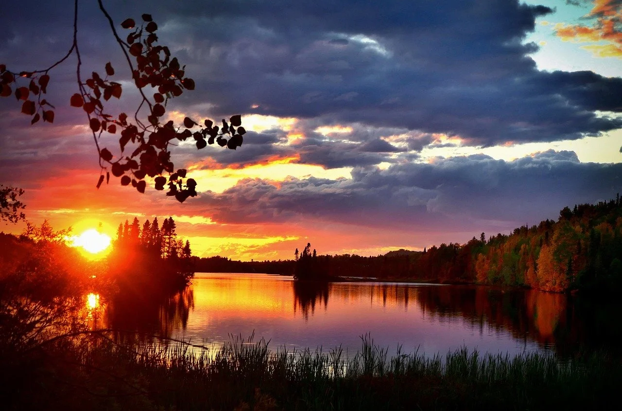 Coucher de soleil sur une rivière bordée d'arbres avec un ciel orageux coloré.