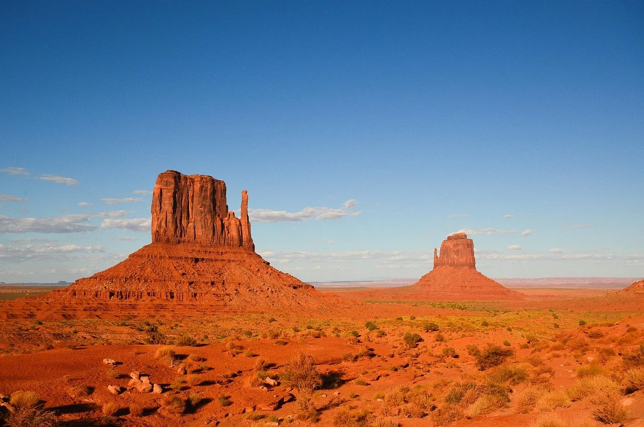 Deux buttes rocheuses rouges dans un désert avec ciel bleu clair et quelques nuages.
