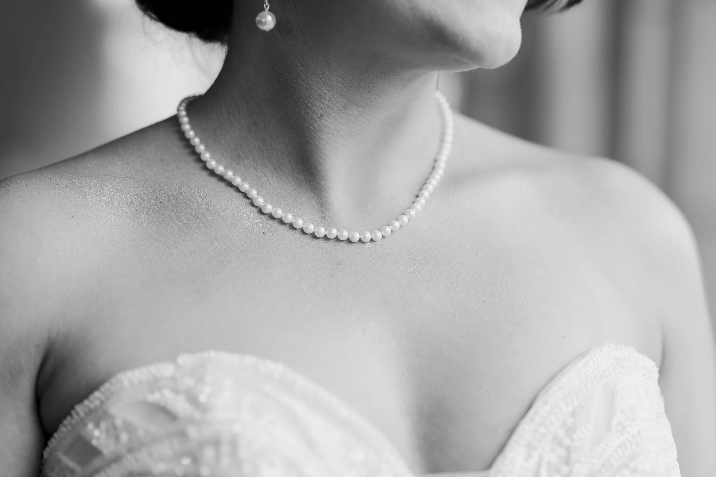 Close-up black and white photo of a woman wearing a pearl necklace and matching pearl earrings, with a strapless dress.