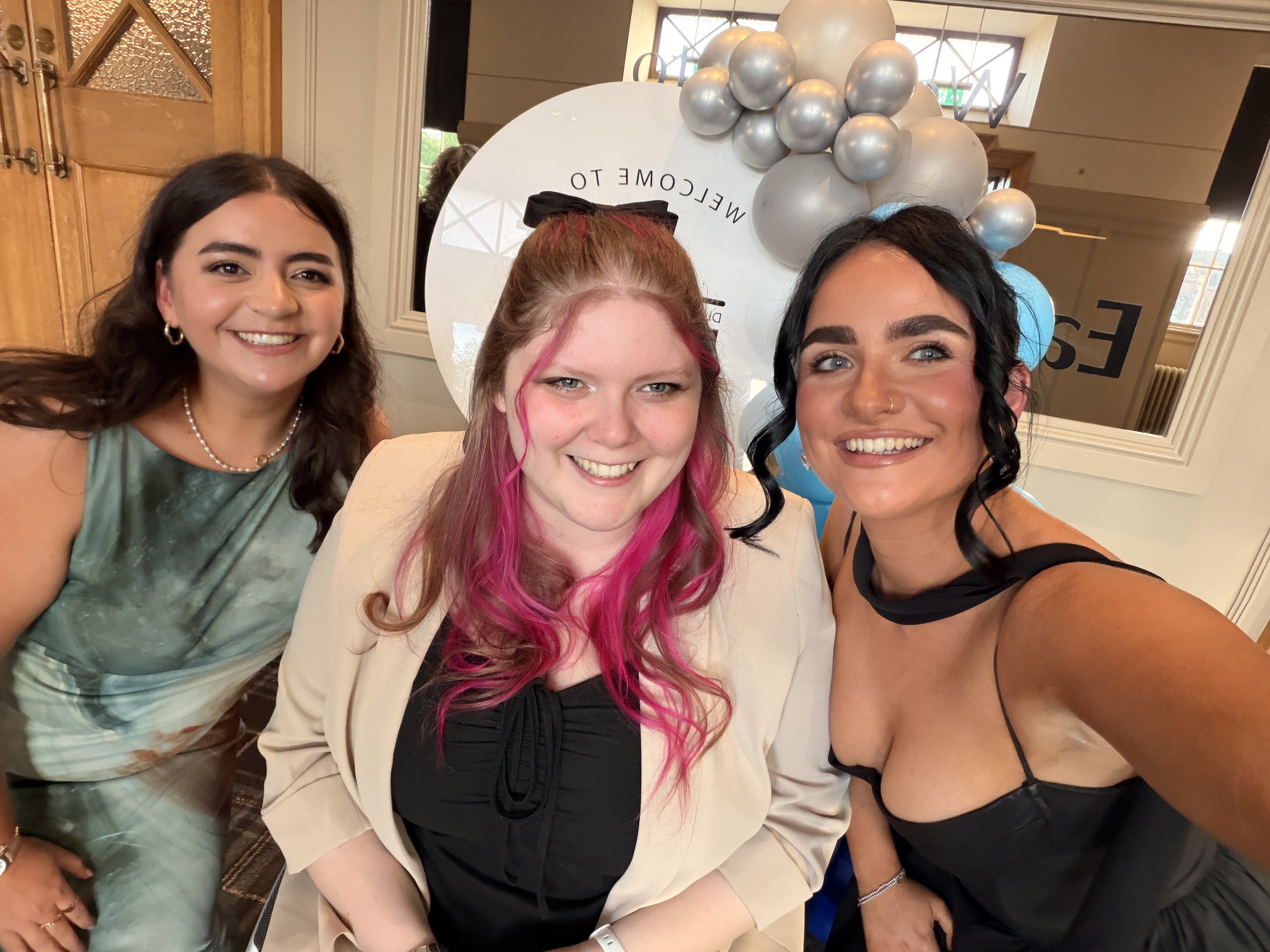 Kara Hunter smiling with two women at a networking event in front of a welcome display and balloon backdrop.