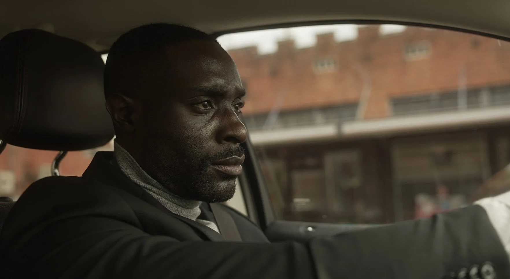 A man driving a car, seen from the passenger seat, with a focused expression on his face.