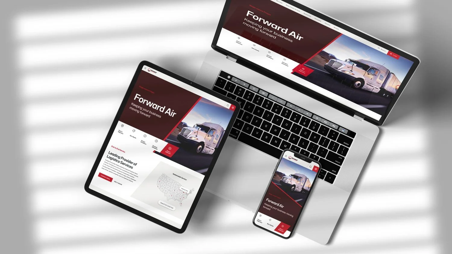 Multiple electronic devices displaying a logistics company's website titled 'Forward Air,' featuring a truck and map graphics, on a white surface with shadows.
