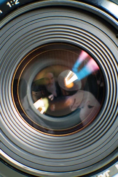 Close-up of a camera lens with reflections of two people taking a photo.