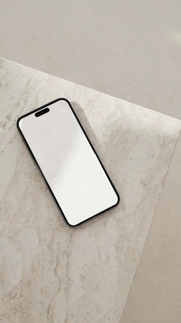 Smartphone with a blank white screen resting on a light-colored marble-textured surface with a gray background.