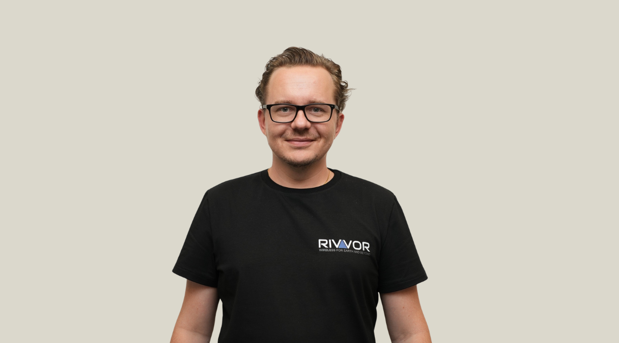A man with glasses and wavy hair wearing a black t-shirt with the RIVR logo and text, standing against a light background.