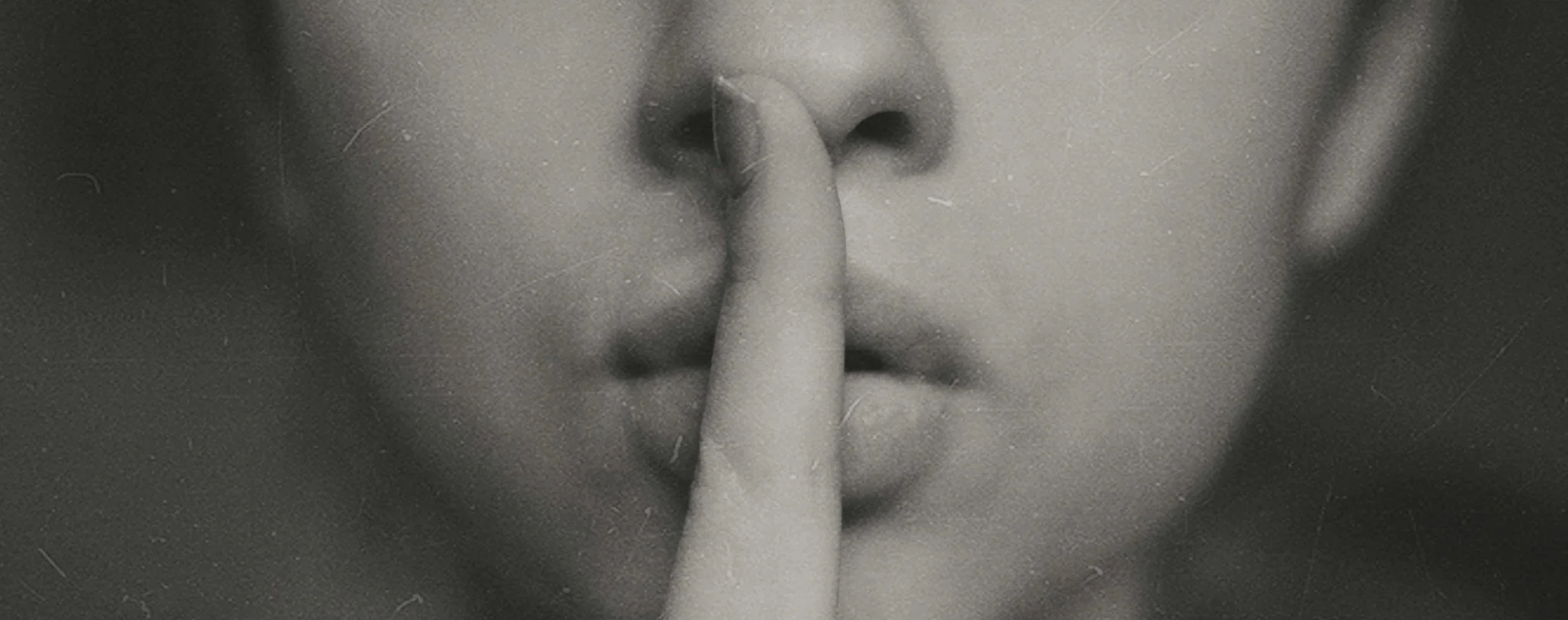 A black & white image of a woman holding a finger over pursed lips