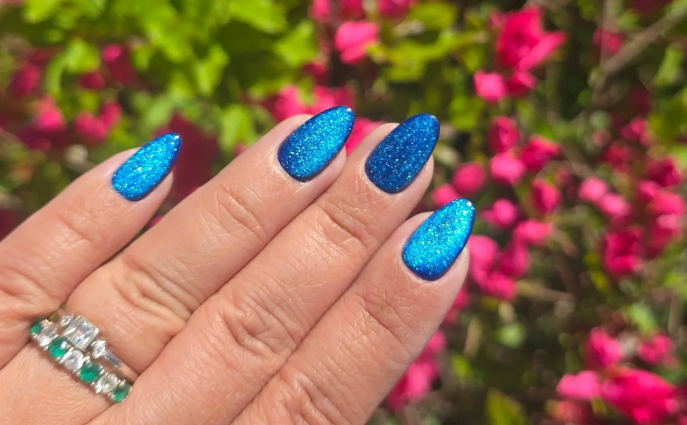 Close-up of a person's hand showing long, almond-shaped blue glittery nails with a sparkly finish