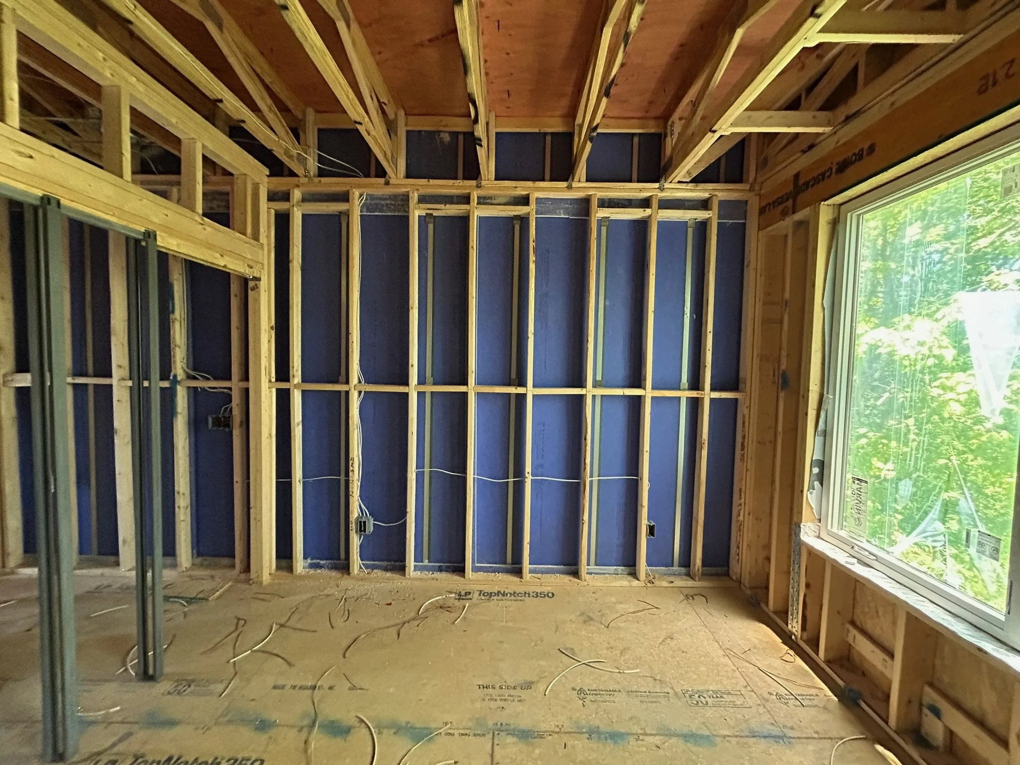 Construction site with worker in green shirt working among wooden framing and electrical wiring.