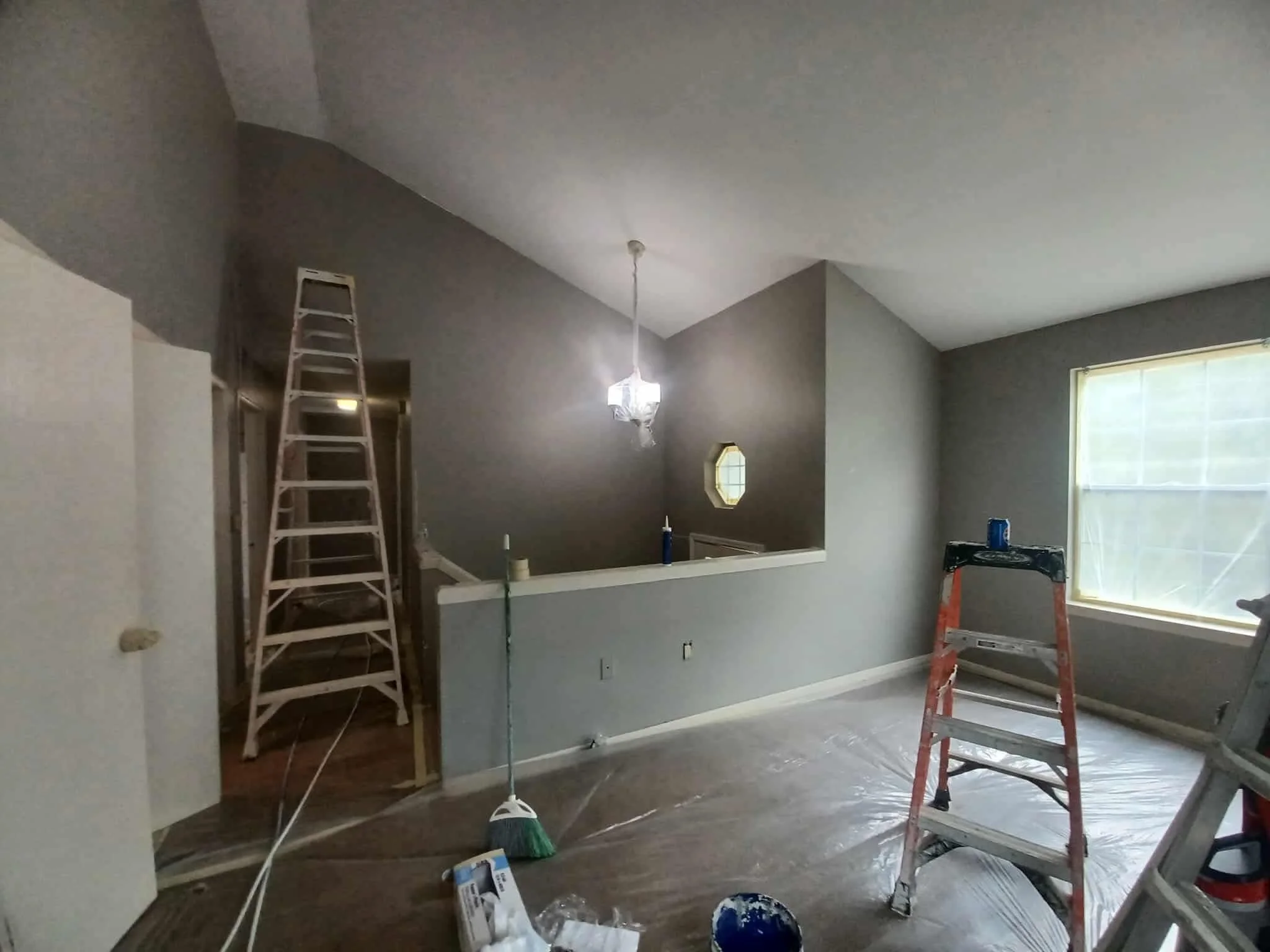 Interior of a house under renovation with ladders, painting tools, and plastic covering on the floor.